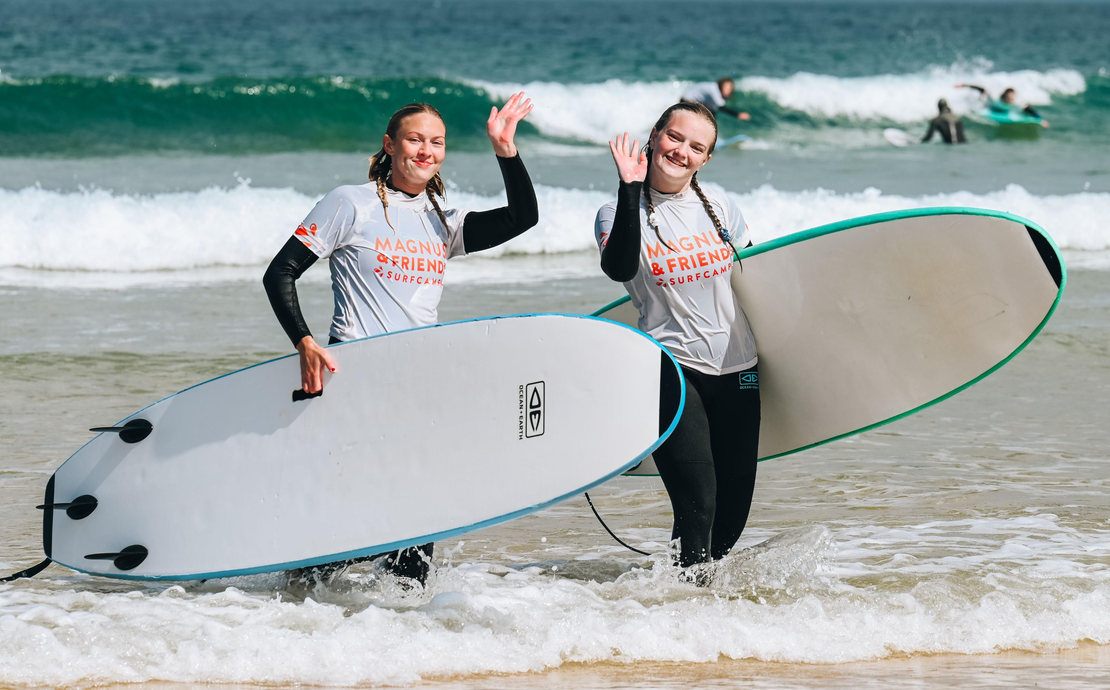 Två glada tjejer som vinkar med surfbrädan