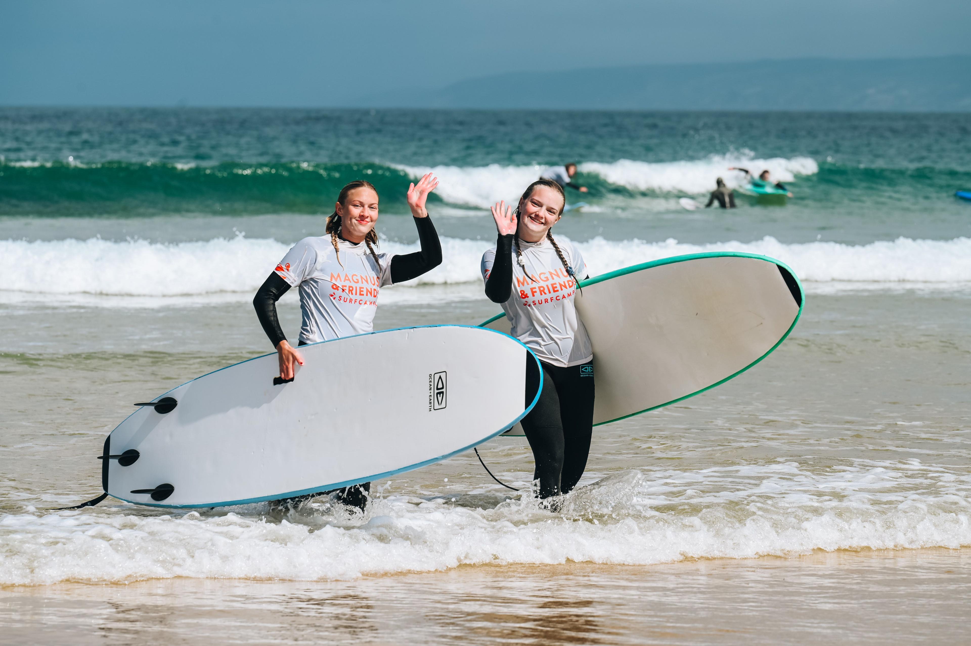 Två glada tjejer vinkar med sina surfbrädor