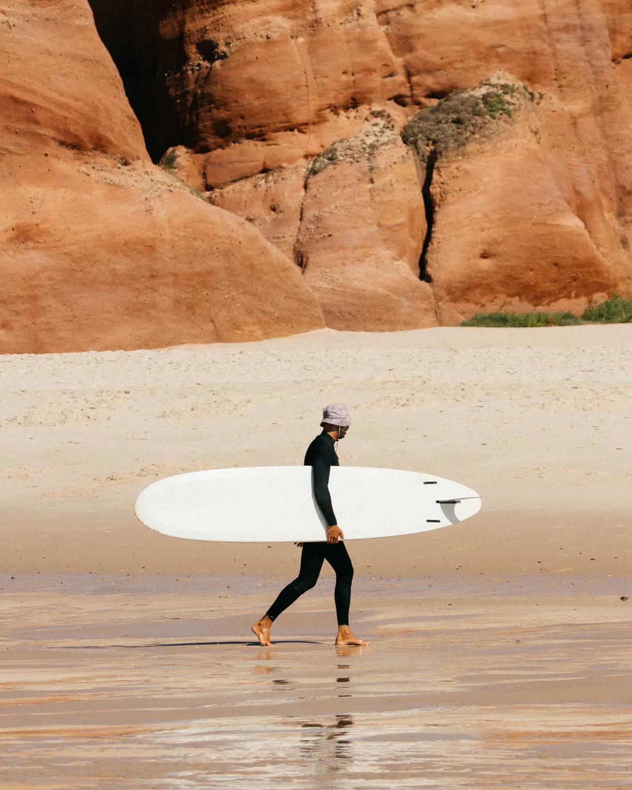 surfare går med surfbräda under armen på stranden