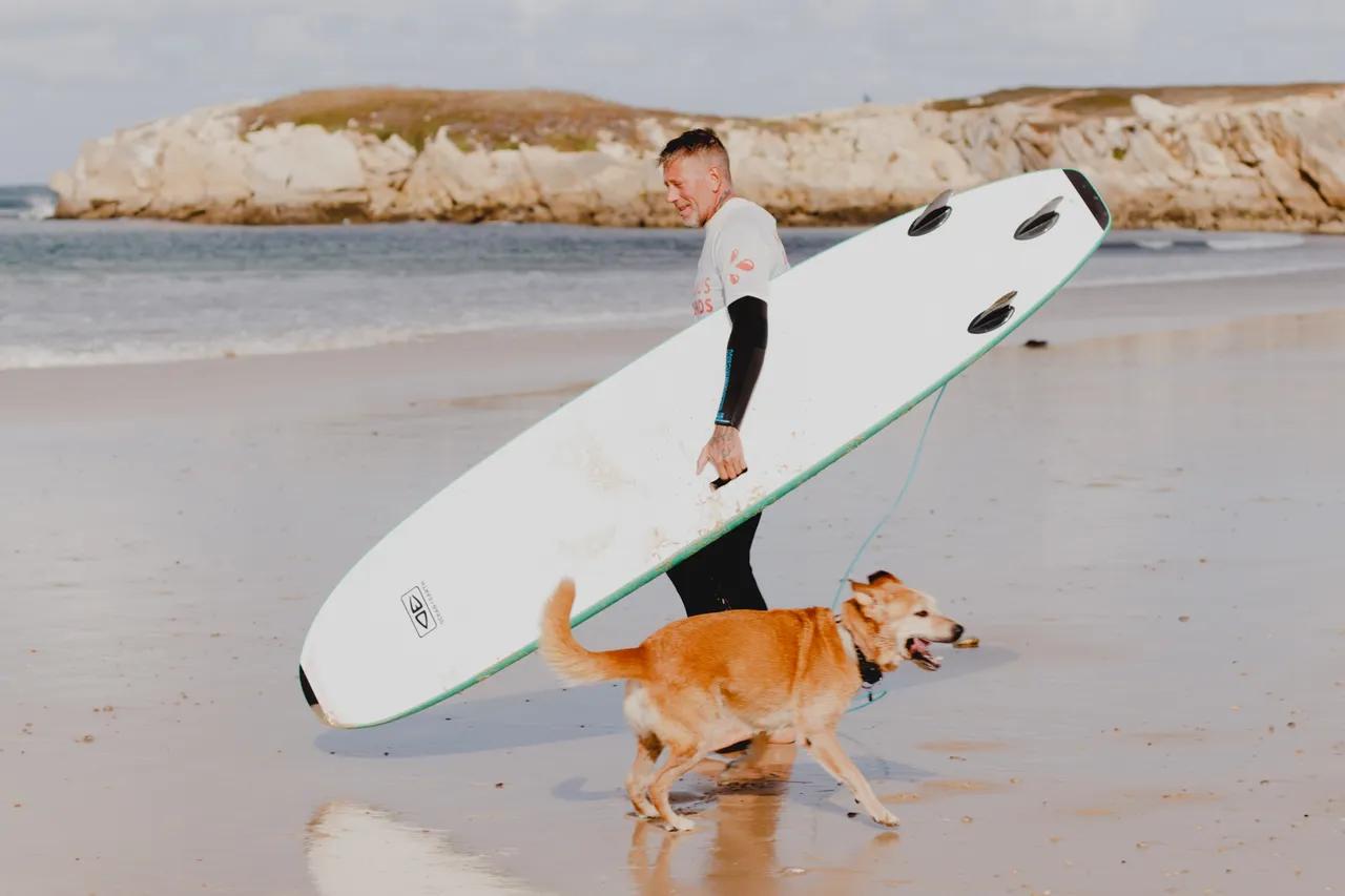 Surfare med bräda på stranden tillsammans med en hund