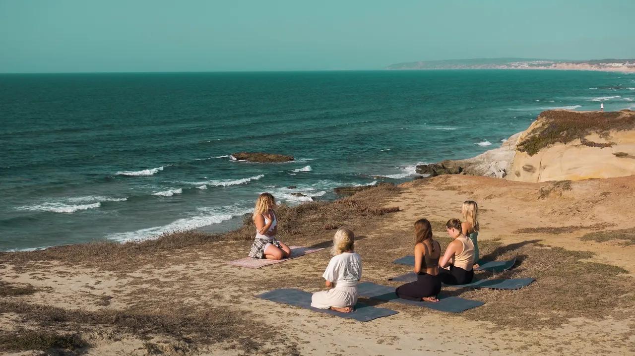 Ett gäng som gör yoga vid klipporna med utsikt över havet
