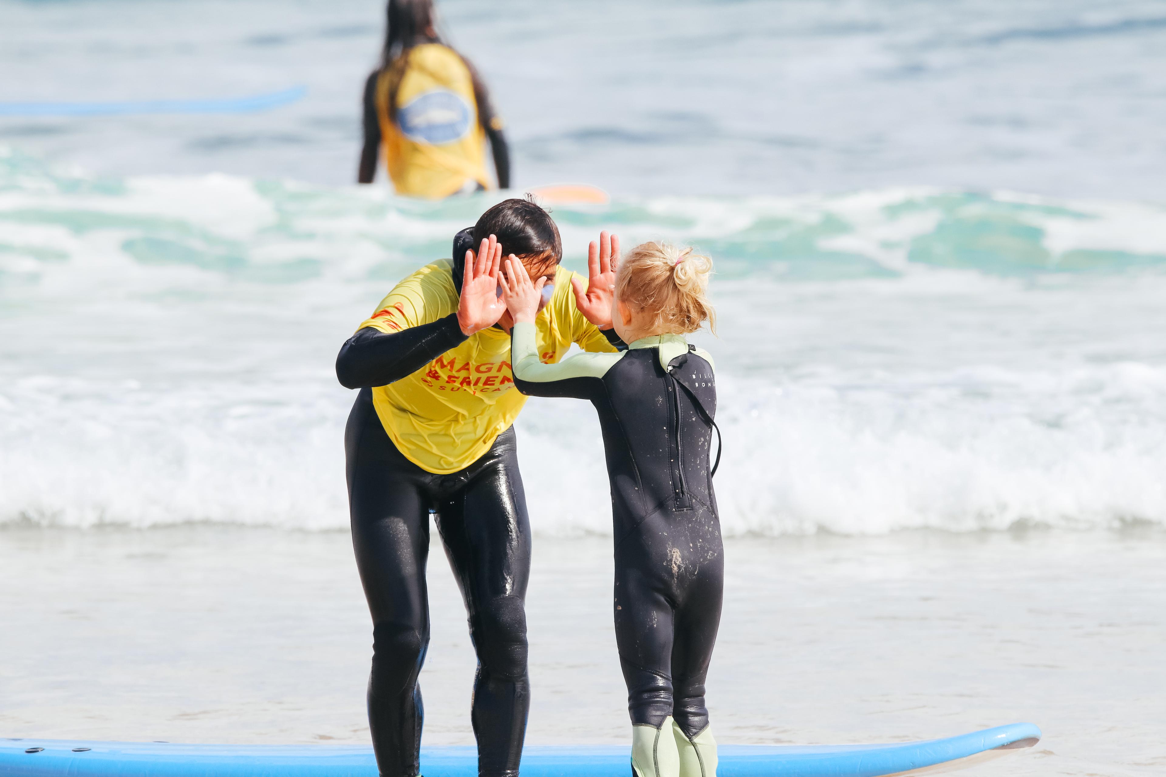 Surfinstruktör Dércio gör highfive med ett barn i vattnet efter hon har surfat en snygg våg