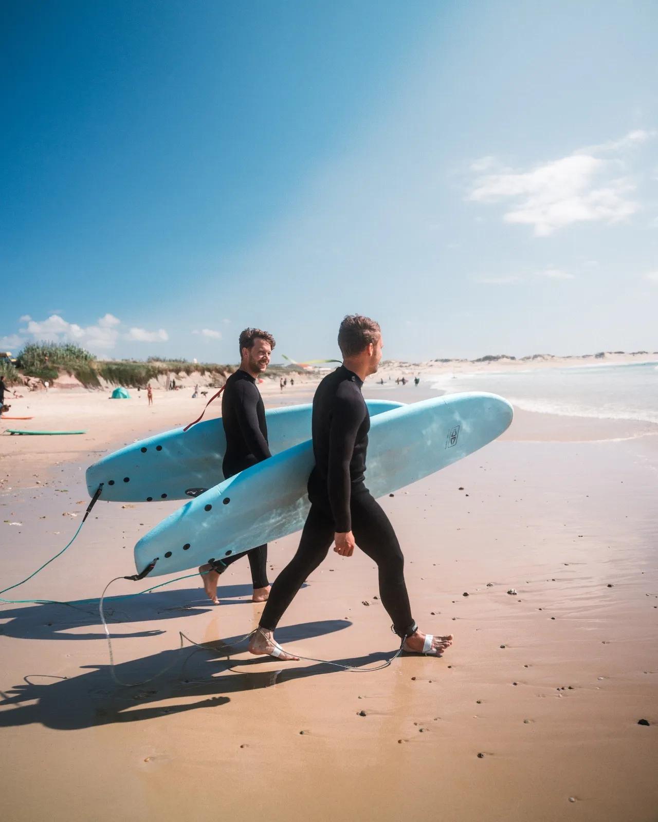 Två surfare med varsin bräda på stranden påväg mot havet