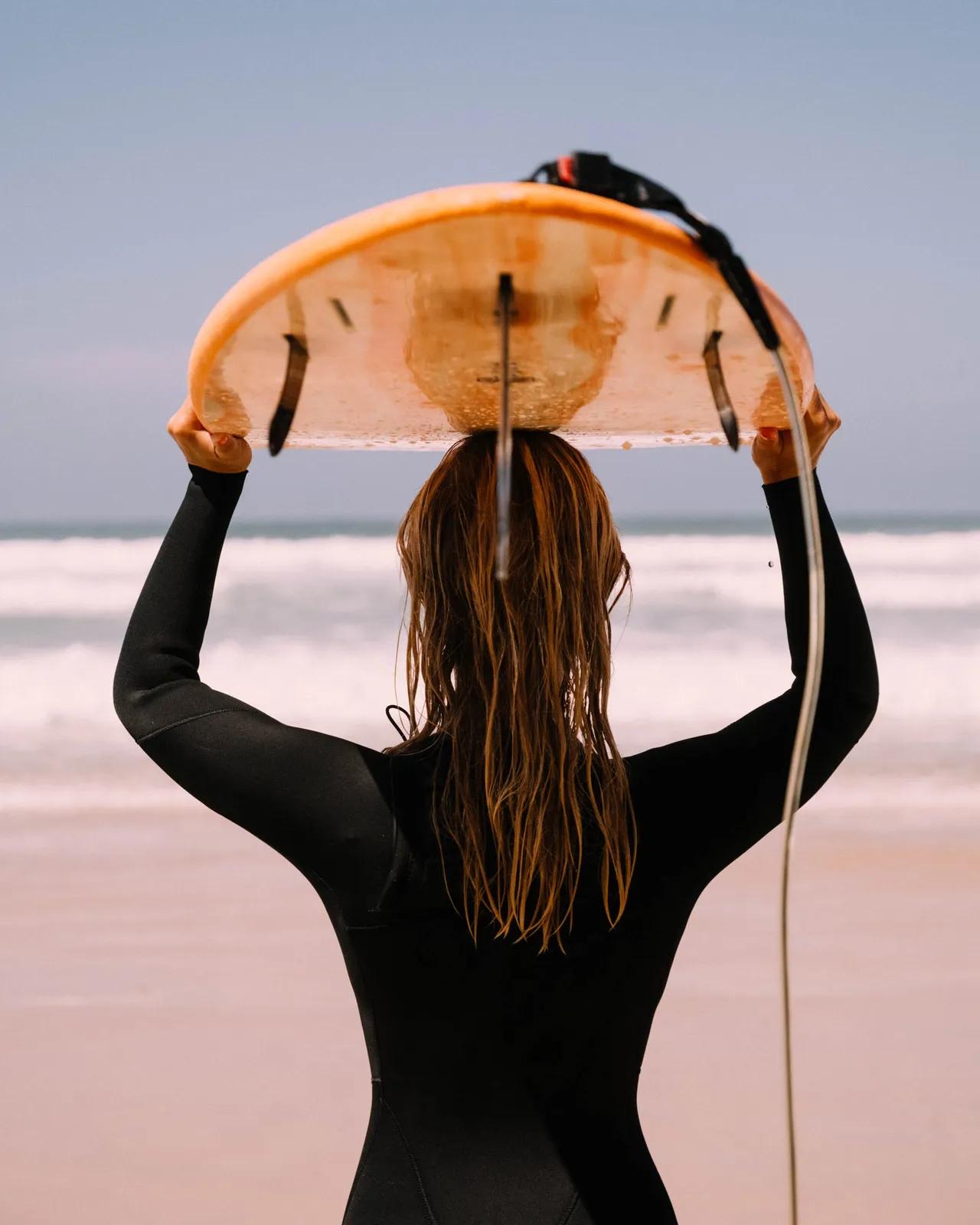 Person bär surfbräda på huvudet och tittar ut mot havet