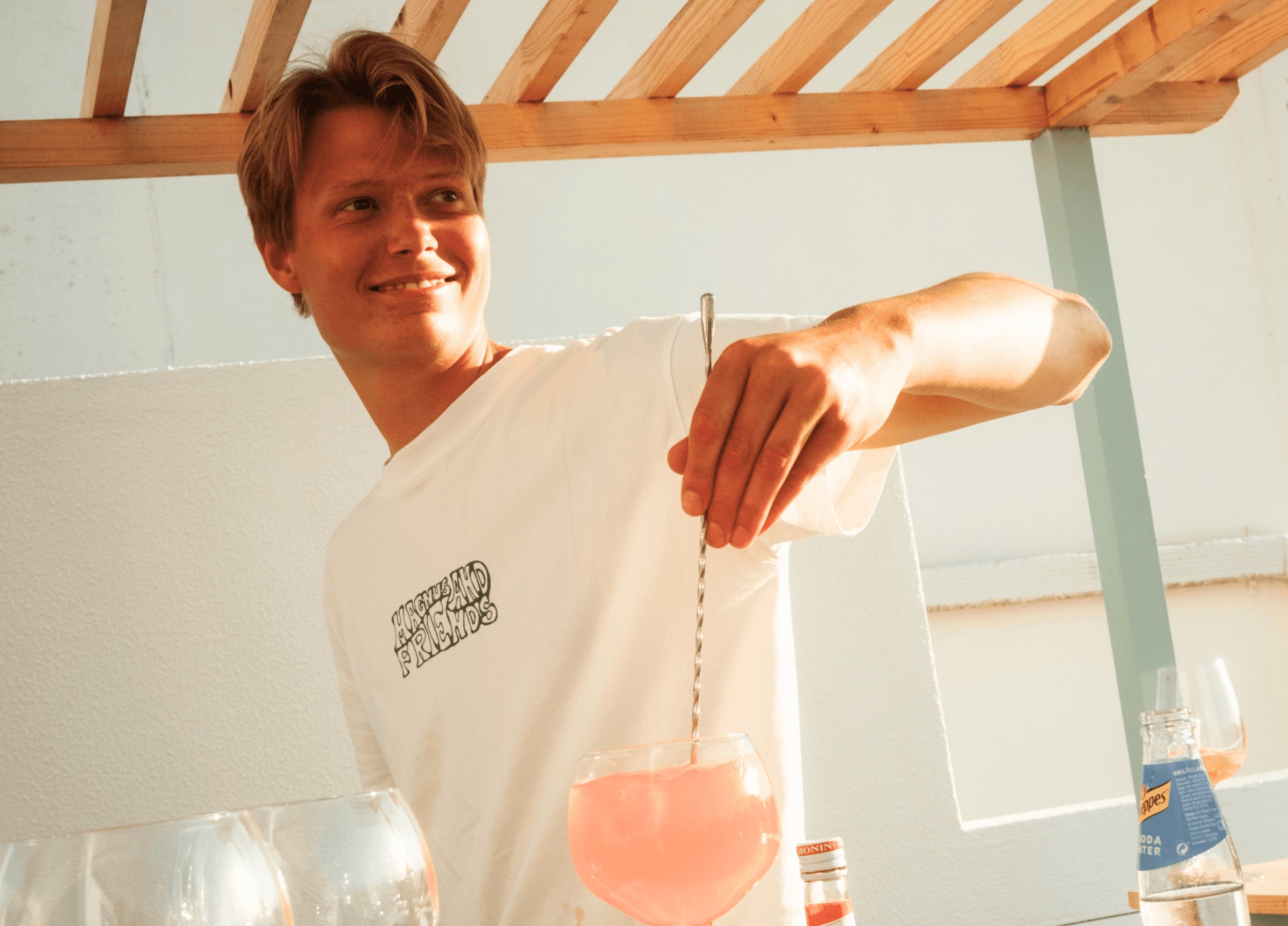 En glad kille som står i baren och gör en drink i eftermiddagssolen.