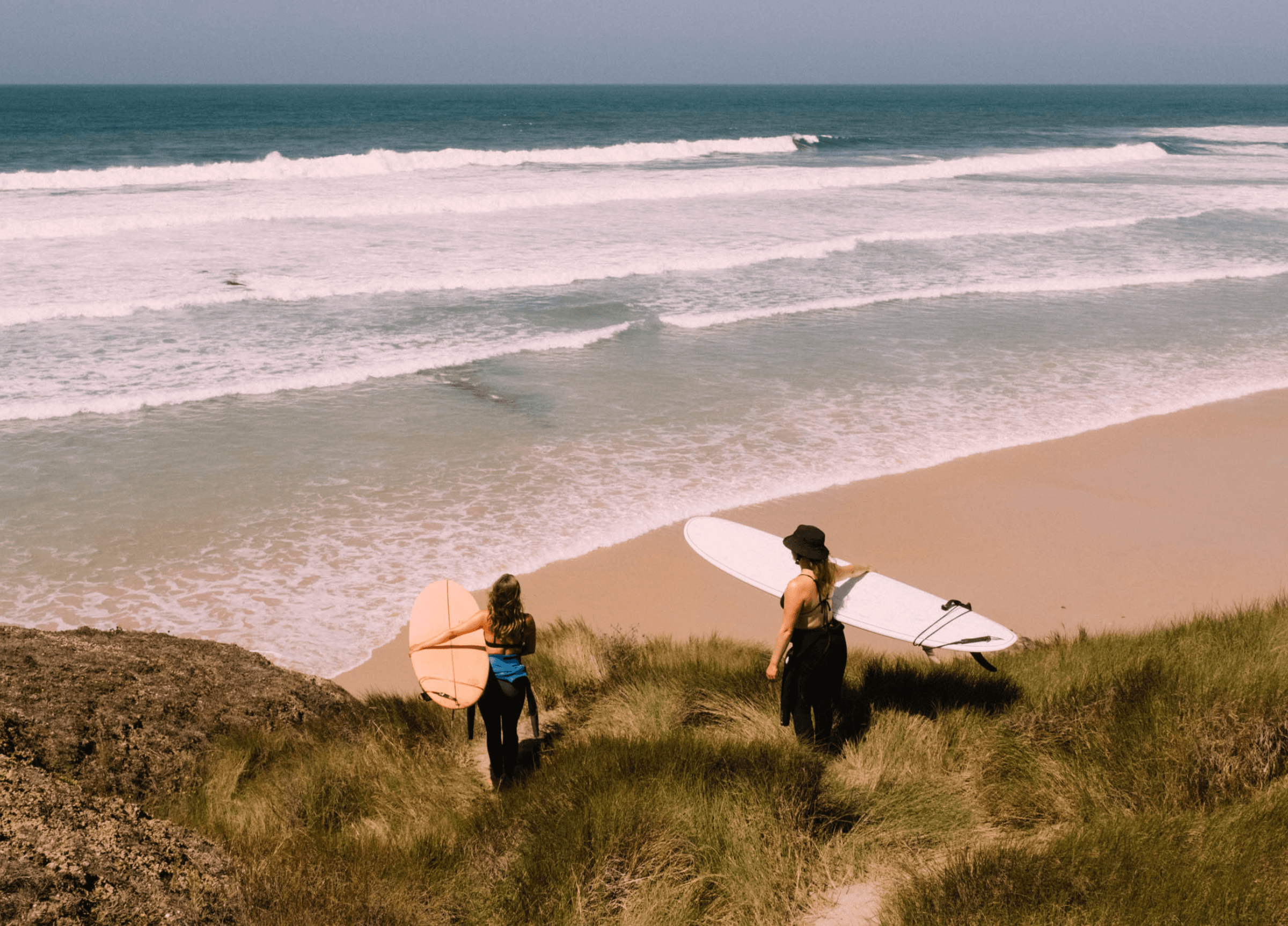 Två surfare påväg ner till havet för att surfa