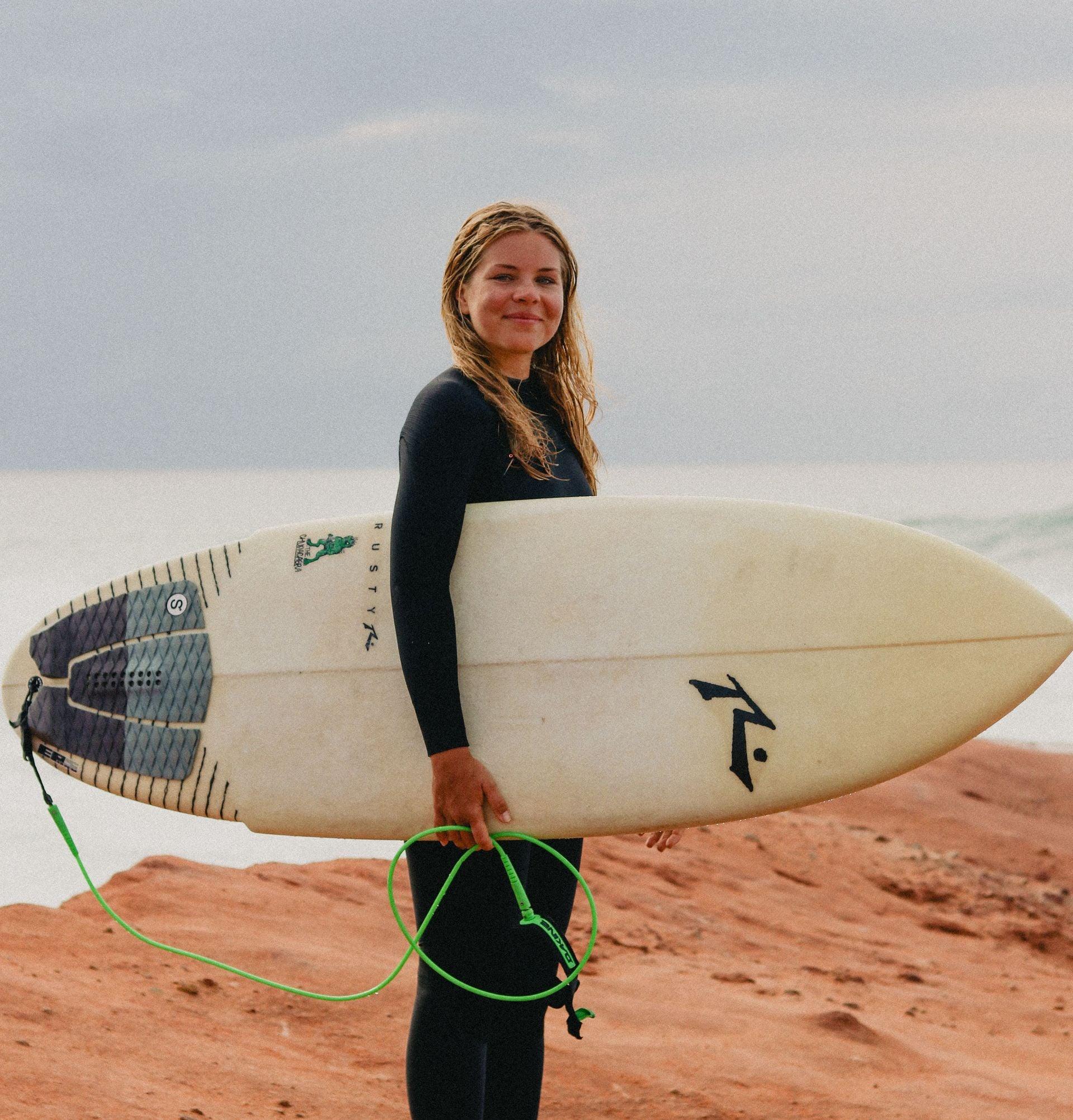Elsa Bergh, camp manager på Magnus & friends med en surfbräda på klipporna