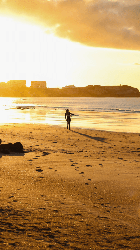 En surfare går längs stranden i solnedgången