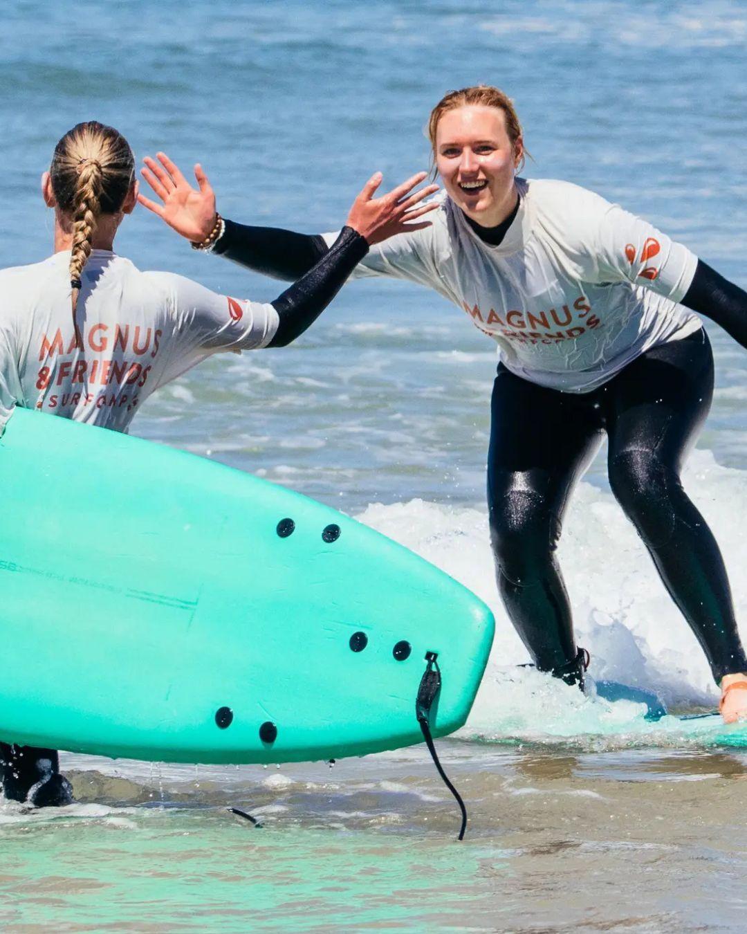 Två tjejer som surfar och gör en high five i vattnet