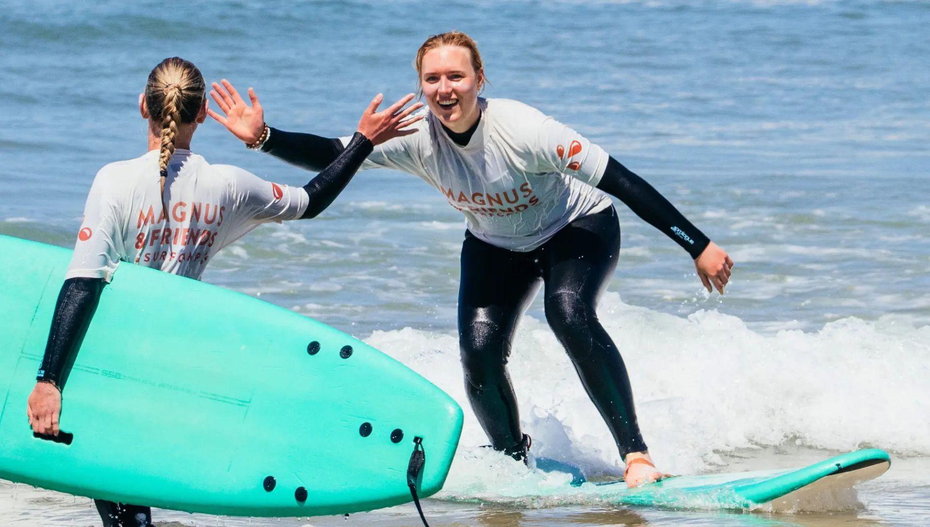 Två tjejer som surfar och gör high five i vattnet.