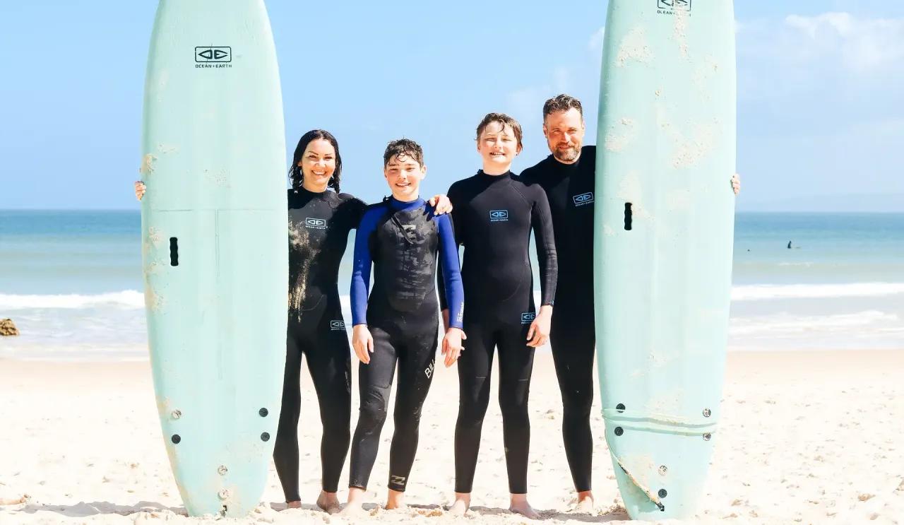 En familj står på stranden med sina surfbrädor och ser glada ut