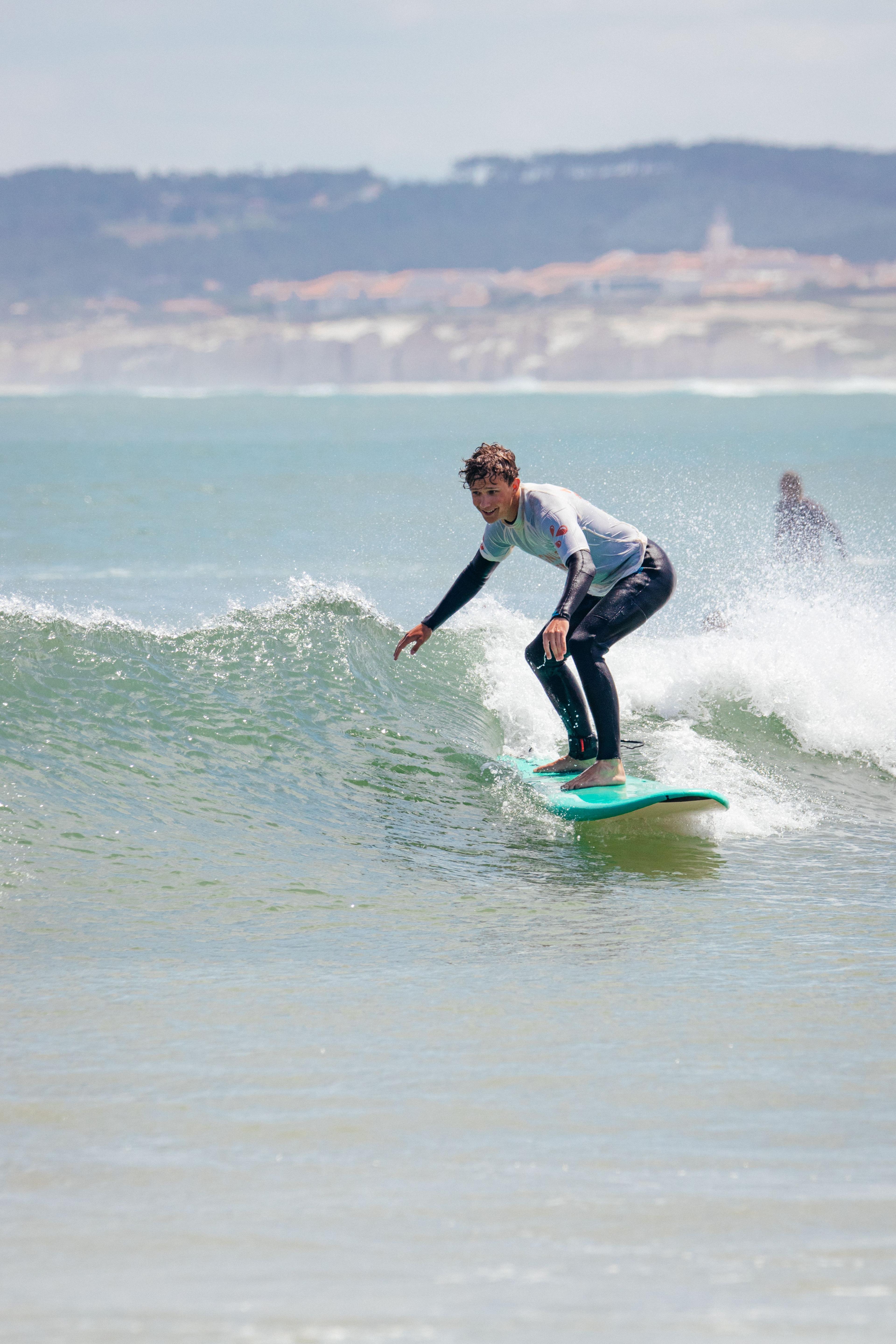 Ung kille som surfar på grön våg med Baleal halvön i bakgrunden