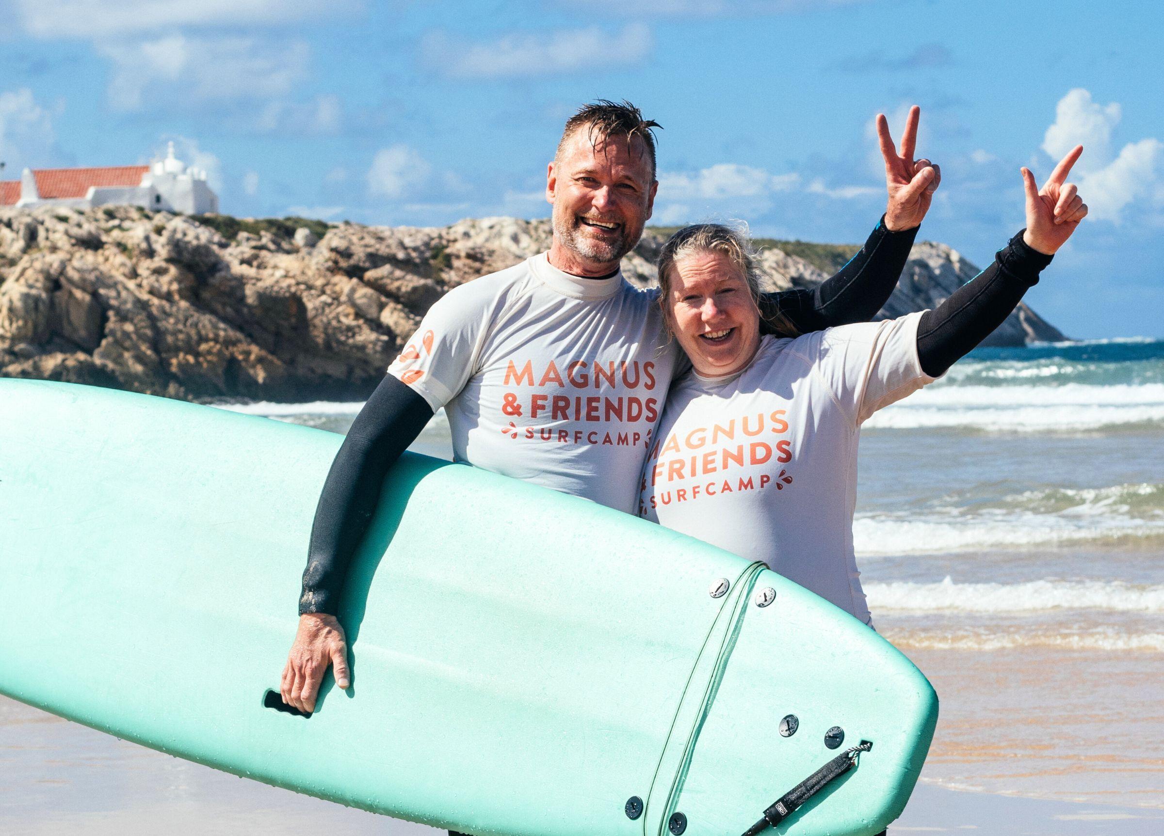En man och kvinna står och poserar på stranden efter deras surflektion.